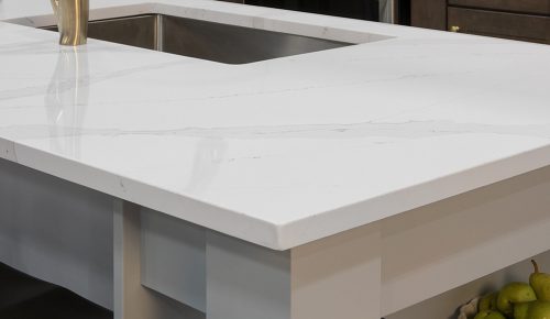 A close-up of a white quartz countertop with subtle veining, an eased edge profile