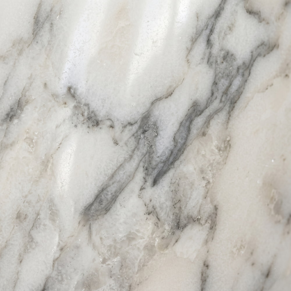 Close-up of polished white marble texture featuring soft, organic gray veining and subtle mineral depth.