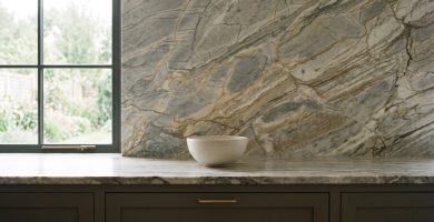 Veined stone countertop and matching full-height backsplash above dark cabinets with brass handles.