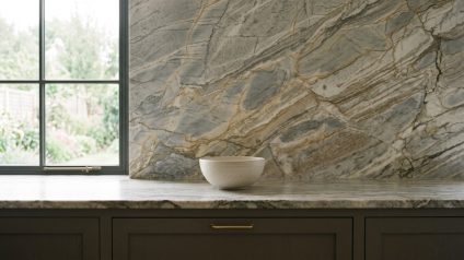 Veined stone countertop and matching full-height backsplash above dark cabinets with brass handles.