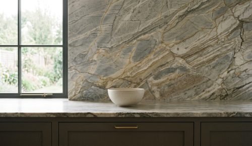 Veined stone countertop and matching full-height backsplash above dark cabinets with brass handles.